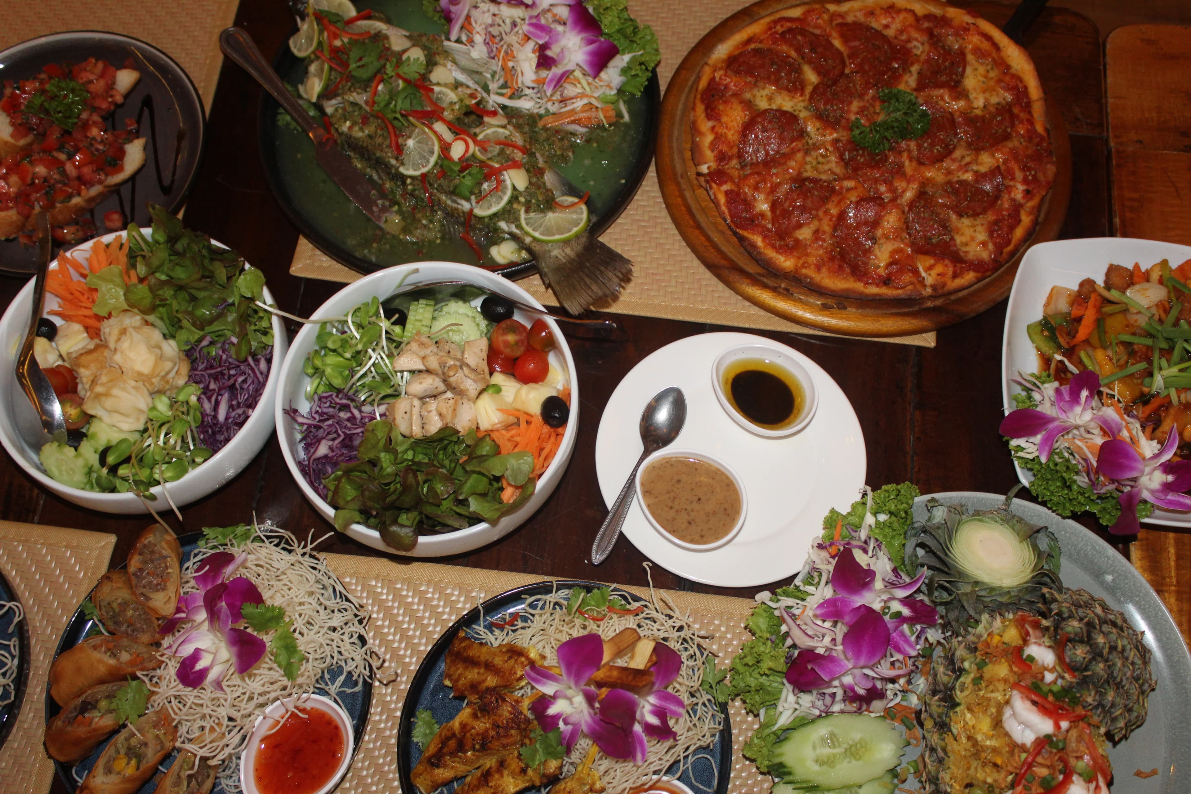 A table at MESA laid with pizza, whole fish, salads, spring rolls and pineapple fried rice